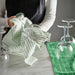 Person cleaning a glass with a green and white striped cloth on a marble surface.