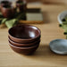 Stack of brown ceramic bowls on a wooden surface with a blurred background