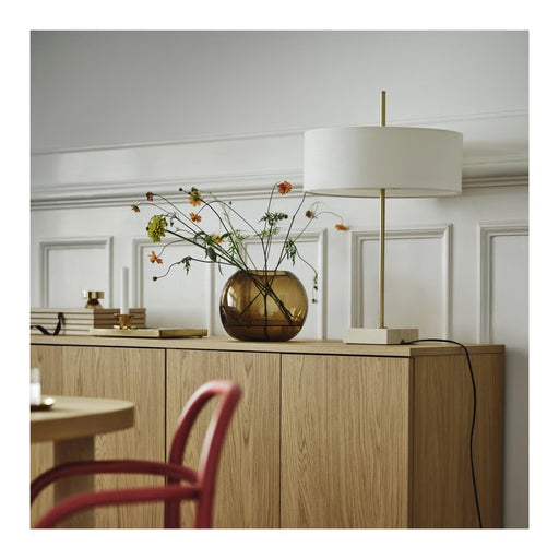 Modern interior with a wooden sideboard, lamp, and vase with flowers.