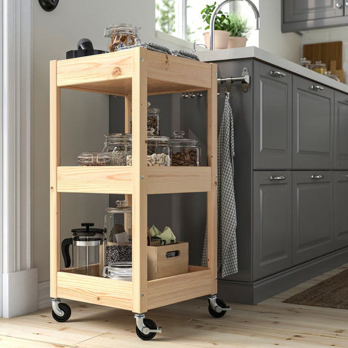  LOSHULT trolley styled in modern kitchen beside grey cabinet, holding glass jars of nuts, seeds, coffee beans, French press, and napkins with dish towel hanging on side rod