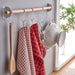 Kitchen utensils and towels hanging on a wooden rod against a light gray wall.