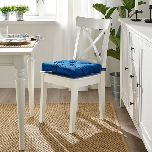 White chair with a blue cushion in a bright room with a table and plants.