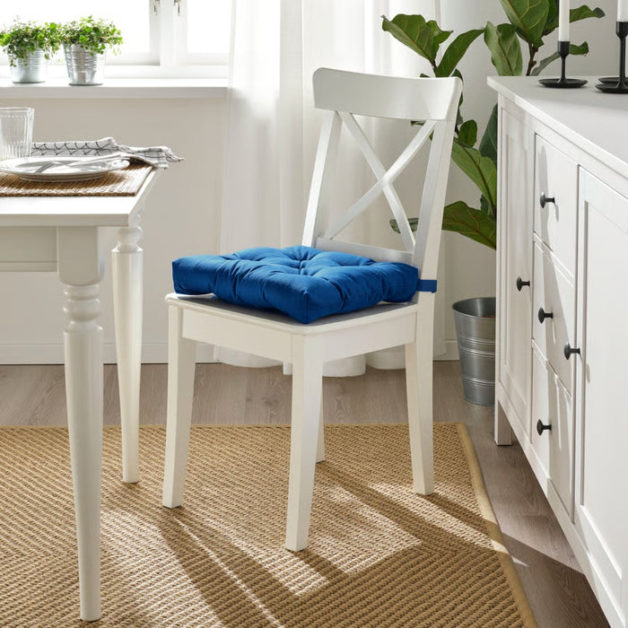 White chair with a blue cushion in a bright room with a table and plants.