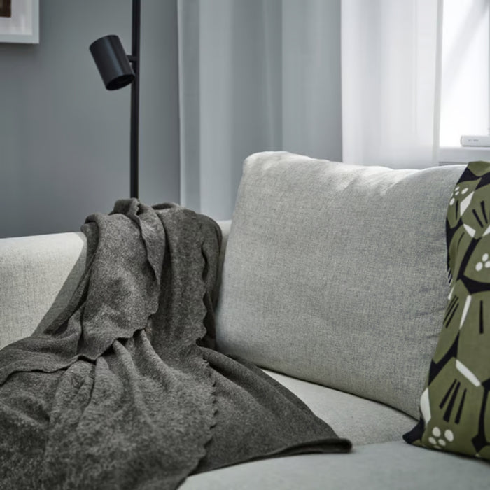 DAGGKÅPOR throw, dark grey, 130x170 cm. Draped over light grey sofa with green patterned cushion and black floor lamp – adds warmth and texture to living room – 50598643.