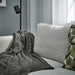 DAGGKÅPOR throw, dark grey, 130x170 cm. Draped over light grey sofa with green patterned cushion and black floor lamp – adds warmth and texture to living room – 50598643.
