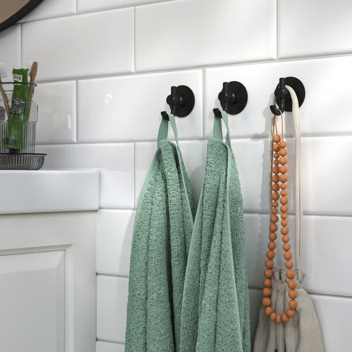 VALASJÖN hooks mounted on white subway tile wall, holding green towels, beige cloth bag, and wooden bead decor
