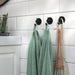 VALASJÖN hooks mounted on white subway tile wall, holding green towels, beige cloth bag, and wooden bead decor
