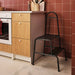 BÄSINGEN 2-step stool with handrail in anthracite, placed beside a red-tiled kitchen cabinet and oven. Ideal for safe access to high shelves in compact kitchen spaces.– 30595754