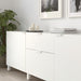 White sideboard with decorative items in a room with a plant and framed pictures.