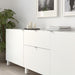 White sideboard with decorative items in a room with a plant and framed pictures.