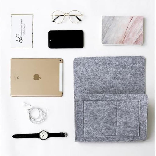 Gray felt laptop sleeve with gold iPad, black phone, marble notebook, glasses, earbuds, and watch on a white background