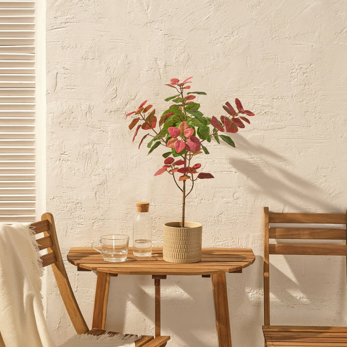 Potted artificial smoke tree placed on a wooden outdoor table in a bright, sunlit setting.