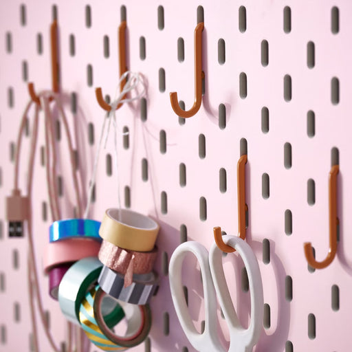 IKEA SKÅDIS hook set in orange (5-pack) mounted on pink pegboard; organizing USB cable, decorative tape rolls, and white scissors – ideal for craft room or office wall storage - 00606136