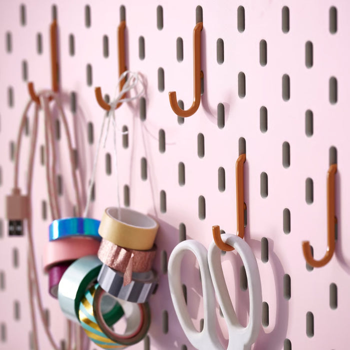 IKEA SKÅDIS hook set in orange (5-pack) mounted on pink pegboard; organizing USB cable, decorative tape rolls, and white scissors – ideal for craft room or office wall storage - 00606136
