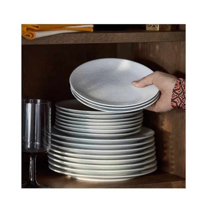 Hand reaching for a stack of white plates from a wooden cabinet.
