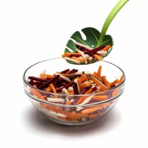 Glass bowl with colorful vegetable sticks and a leaf-shaped spoon on a white background