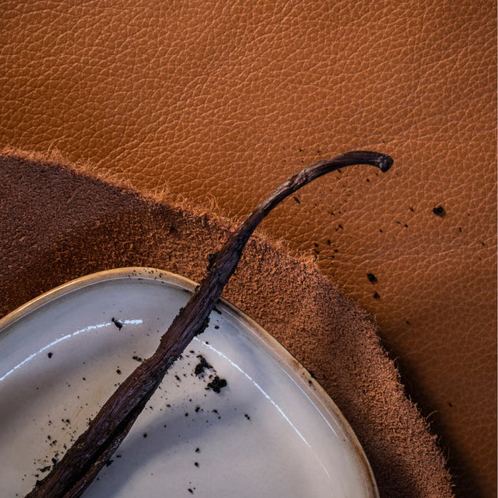 Close-up of vanilla bean pod on white ceramic dish over textured brown surface, evoking IKEA SILKESTRÄD scented tealight’s leather and vanilla fragrance – 3.5-hour burn time, 30-pack - 20570551