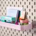 Pink shelf with stationery items against a pegboard wall