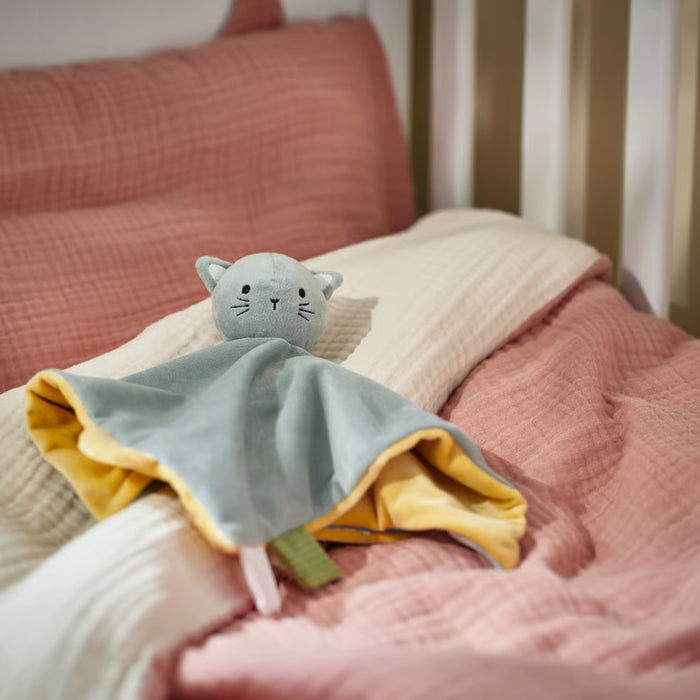 Blue and yellow cat-shaped comfort blanket placed on pink bedding in a cozy crib setting.