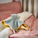 Blue and yellow cat-shaped comfort blanket placed on pink bedding in a cozy crib setting.