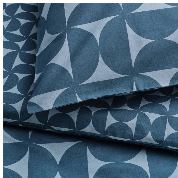 Close-up of IKEA ÄNGSNEJLIKA pillowcase fabric with overlapping circular and pointed geometric shapes in shades of blue and light gray, highlighting texture and design.

