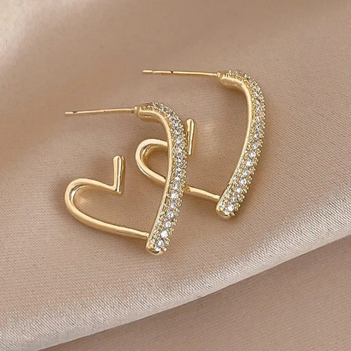 Gold heart-shaped earrings with clear stones on a beige background