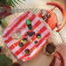 Top-down view of the pink and red striped potting mat used on a table for indoor gardening with soil and small plants.