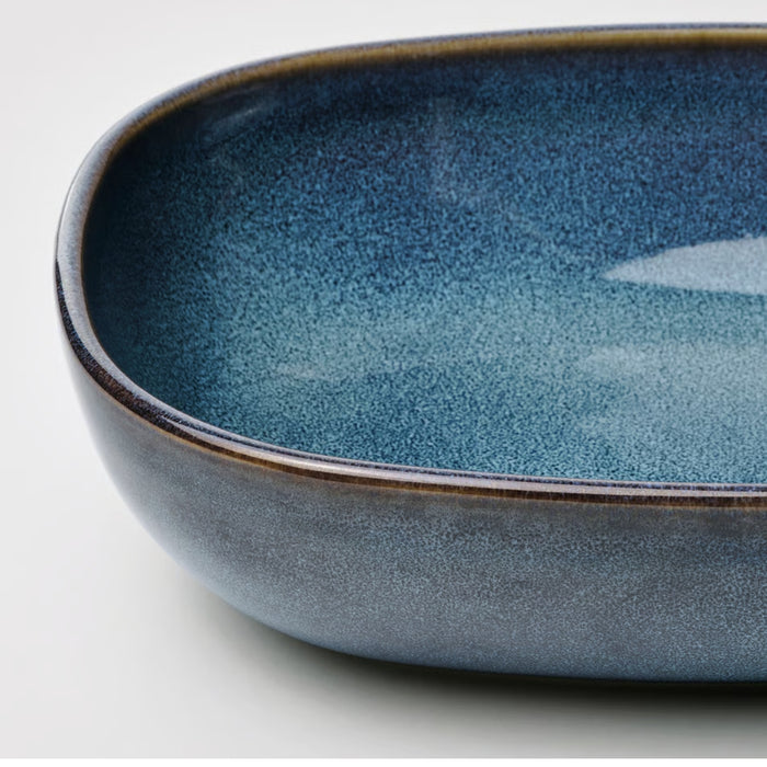 Close-up of an oval ceramic oven dish from the IKEA GLADELIG set, showcasing its rich blue color and glossy finish. The bowl features a smooth, curved silhouette with a gradient transitioning from dark to light blue, both inside and out. The reflective glaze enhances its elegance, making it suitable for both cooking and serving directly at the table -20531079.