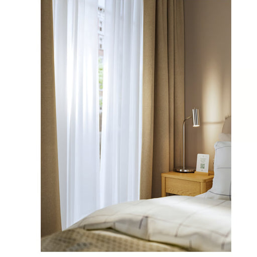 Bedroom with brown curtains, white bedding, and a nightstand with a lamp.