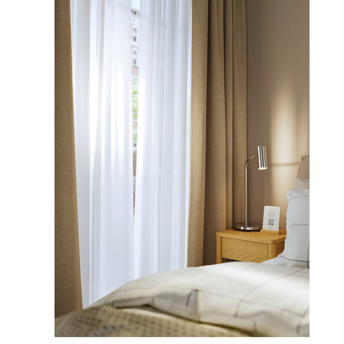 Bedroom with brown curtains, white bedding, and a nightstand with a lamp.