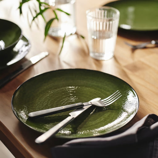 Close-up of a green PELARKAKTUS side plate with a silver fork and black-handled knife on a wooden dining table.