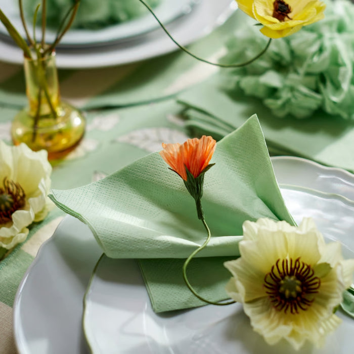 A decorative table setting featuring a light green paper napkin folded elegantly on a white plate with artificial flowers.
