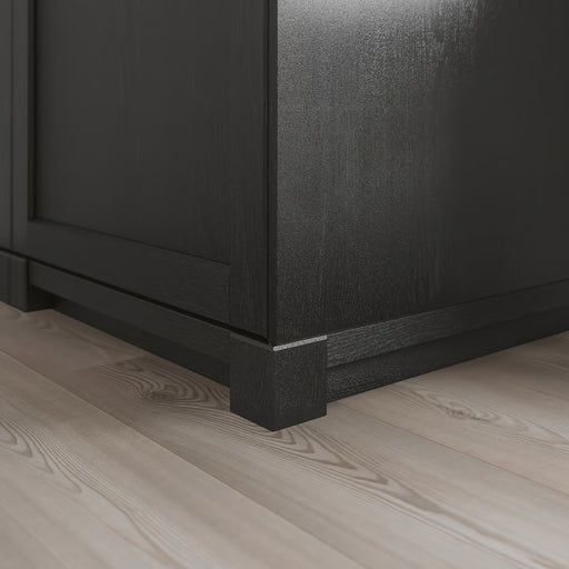 Close-up of a black wooden cabinet corner on a light wood floor.