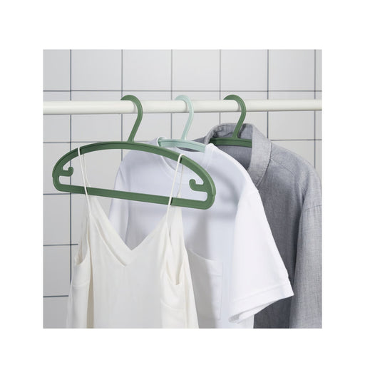 Green hangers with clothes on a white rack against a tiled wall.
