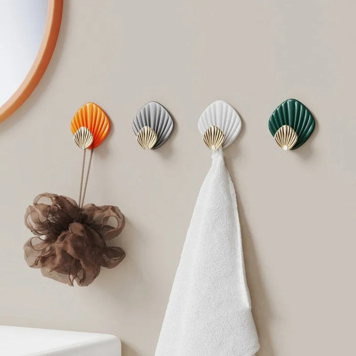 Four shell-shaped wall hooks in different colors with a towel and bath sponge hanging on them.