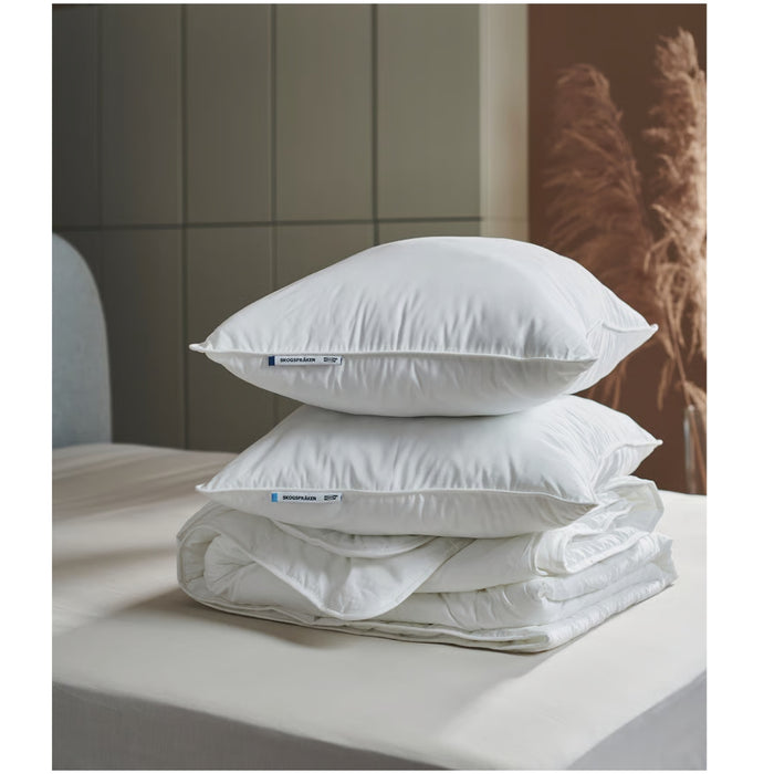 Stack of white pillows and duvet on a bed with a neutral background