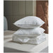 Stack of white pillows and duvet on a bed with a neutral background