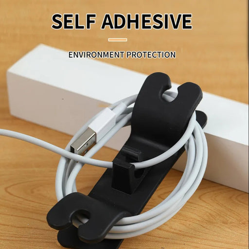 Black cable clip holding white cables with text 'Self Adhesive' and 'Environment Protection' on a wooden surface.