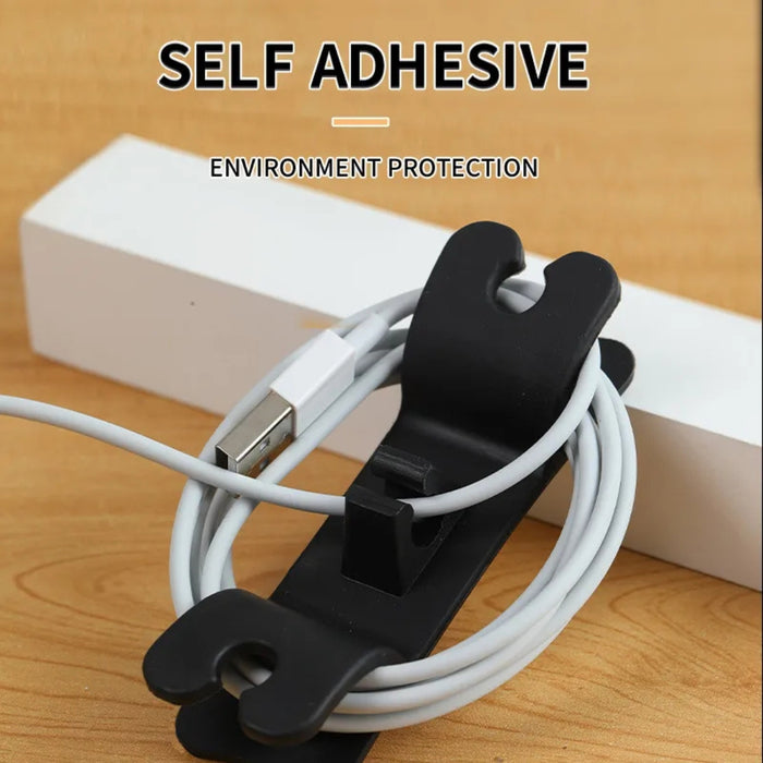 Black cable clip holding white cables with text 'Self Adhesive' and 'Environment Protection' on a wooden surface.