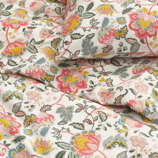 Detailed view of floral-patterned bedding with large pink, yellow, blue, and green flowers and green leaves on a white cotton fabric.

