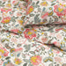 Detailed view of floral-patterned bedding with large pink, yellow, blue, and green flowers and green leaves on a white cotton fabric.


