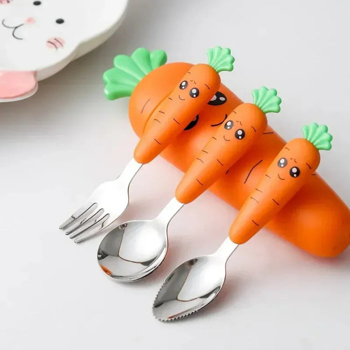 Children’s carrot-themed tableware set featuring a trio of utensils—fork, spoon, and serrated spoon—each with fun orange handles shaped like smiling carrots with leafy green tops; set is placed on a large carrot-shaped holder with matching playful faces. In the background, a cat-face shaped plate adds to the whimsical, kid-friendly presentation – 1600002332714 12850097.