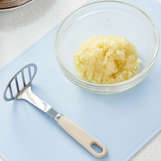 Stainless steel potato masher – mashed potatoes in glass bowl with masher placed on blue countertop