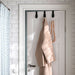 IKEA VALASJÖN hanger in use on a white bathroom door, holding a beige bathrobe and wooden bead decor beside a patterned shower curtain