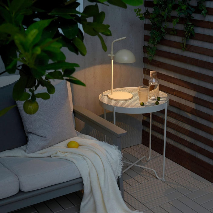 IKEA SOMMARLANKE decorative table lamp in beige placed on white mesh table in cozy outdoor seating area; soft ambient glow beside water bottle, glass, and green fruits – ideal for patio or balcony decor - 20544821