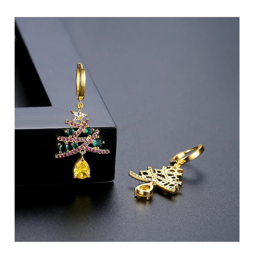 Gold earrings with tree and leaf designs on a dark surface