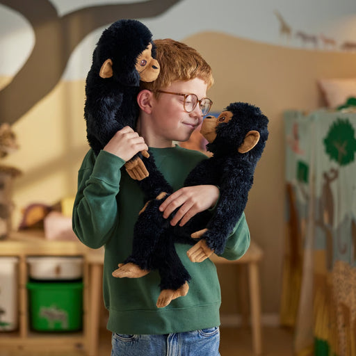 Child holding two SANDLÖPARE chimpanzee toys in playroom with animal-themed wall decor and storage bins