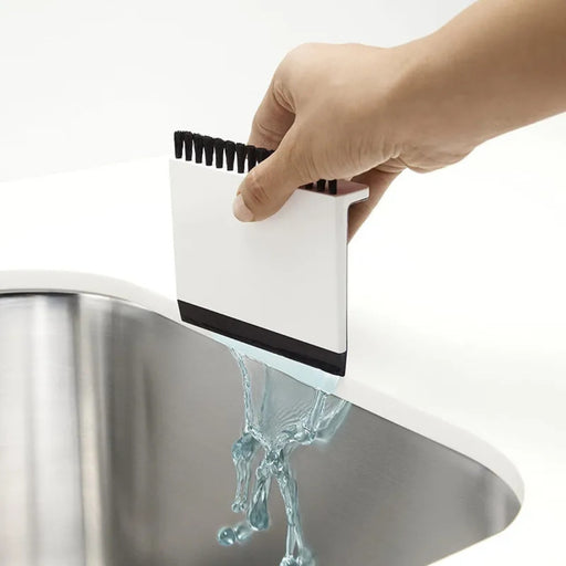 Hand using a white scrubber with black bristles to clean a stainless steel sink.