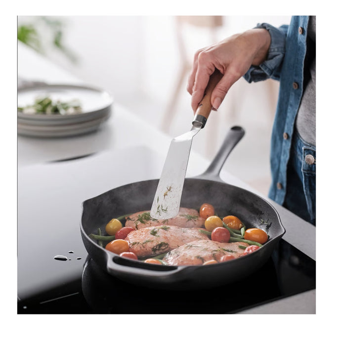 Person cooking in a kitchen with a cast iron skillet on a stove