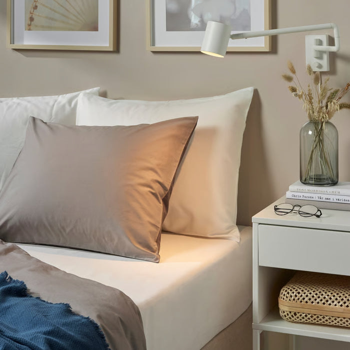 Neatly made bed with pillows and a nightstand with a lamp and vase.